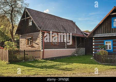 Komposition von zwei historischen Blockhäusern mit dunkler Holzfassade, Schindeldach und Zaun im Dorf Osturňa. Stockfoto