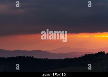 Blick auf die Maly Rachowiec-Bergkette bei Sonnenuntergang mit geschichteten Silhouetten, dunklen Wolken und lebhaftem orangefarbenem Licht in Zwardon, Woiwodschaft Schlesien, Polen Stockfoto