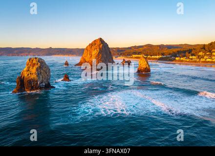 Ein atemberaubender Blick aus der Luft auf Haystack Rock und die Cannon Beach Küste, getaucht in das warme, goldene Licht eines lebendigen Sonnenuntergangs über dem Pazifik Stockfoto