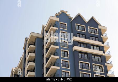 Blaues Wohngebäude mit moderner Architektur, das mehrere Stockwerke, Fenster und Balkone aufweist und zeitgenössisches Stadtleben und Wohnraum bietet Stockfoto