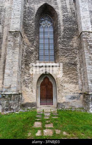 Tallinn, Estland – 2. Oktober 2026: Ein spitzer Steinbogen umgibt eine Holztür unter einem hohen Kirchenfenster, mit Gras und einem Steinpfad im Vordergrund Stockfoto