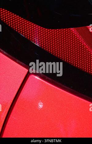 detaillierte Makrofotografie, die sich auf eine strukturierte rot lackierte Metalloberfläche neben einem gemusterten roten Rücklichtelement mit weicher Beleuchtung konzentriert. Stockfoto