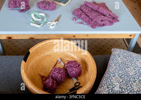 Rosa gestrickte Wollstücke und Wollknäuel in einem Korb auf einem Wohnzimmertisch. Stockfoto