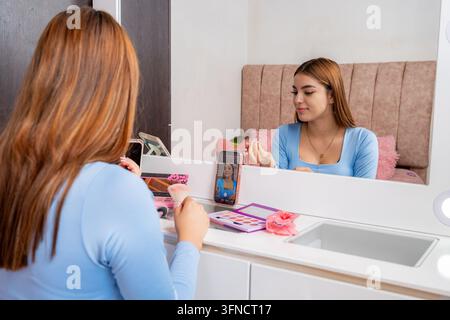 Junge Frau, die sich im Spiegel betrachtet und für ihre Follower ein Online-Beauty-Make-up-Tutorial mit einem Smartphone aufnimmt, wobei sie digitales Con erstellt Stockfoto