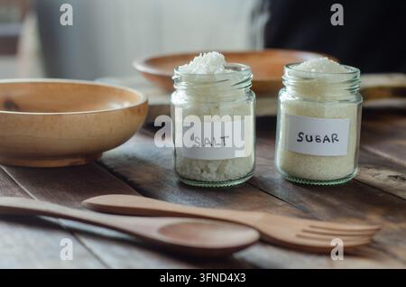 Zwei Gläser enthalten Salz und Zucker, klar beschriftet. Holzschalen und Utensilien ruhen in der Nähe, rustikal und einfach. Weiches Licht umspült die Szene, sanft und einladend Stockfoto