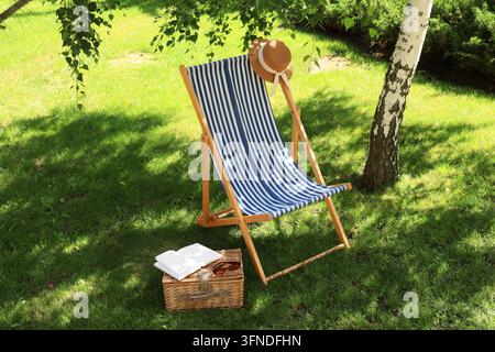 Arbeits-Lebens-Gleichgewicht und Sommerurlaub, leerer Liegestuhl mit Strohhut und Buch auf Picknickkorb in sonnigem Garten für Entspannung und Freizeit Stockfoto