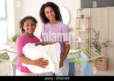Familienpflichten und Haushaltsverantwortung, Mutter und Tochter waschen zusammen zu Hause Wäsche mit einem Korb voller sauberer Kleidung in einem hellen Wohnzimmer Stockfoto