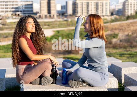 Zwei Frauen in Sportkleidung entspannen und kommunizieren nach dem Training im Freien Stockfoto