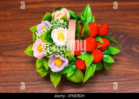Zartes Bouquet aus Seife in Form von Blumen und Erdbeeren in einem Holzkorb auf braunem Hintergrund. Exklusive Handarbeit. Stockfoto