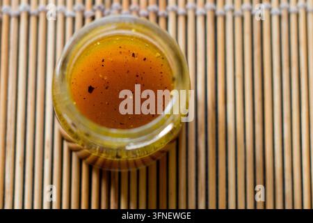 Oberansicht von goldenem Honig mit dunklen Gewürzflecken in einem offenen Glasgefäß auf einer Bambusmatte, geringe Tiefenschärfe, Nahaufnahme-Foodfotografie Stockfoto