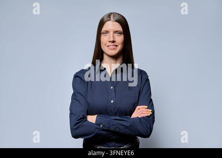 Selbstbewusste 30-jährige Geschäftsfrau mit verschränkten Armen auf grauem Hintergrund Stockfoto