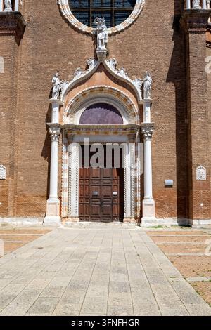 Nahaufnahme einer historischen Ziegelsteinkirchenfassade mit geschnitztem Steinornament, Skulpturenfiguren, gewölbten Fenstern, Säulen und einem dunklen hölzernen Eingang. Stockfoto