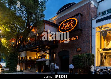 Mexico-Stadt, Mexiko - 23. August 2026: Nachtansicht von außen des gehobenen Ziegelrestaurants Puerto Madero mit Neonzeichen und abendlichen Gästen in Polanco. Stockfoto