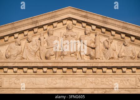 Giebeldetail am Obersten Gerichtshof | WASHINGTON — Skulpturale Figuren füllen das Westgiebel des Obersten Gerichtshofs der Vereinigten Staaten auf dem Kapitolhügel in Washington, D.C. Der Bildhauer Robert Aitken betitelte das Relief „Gleiche Gerechtigkeit unter dem Gesetz“ und konzentrierte sich auf eine thronende Freiheit, flankiert von Ordnung und Autorität, mit Gruppen, die Rat und Forschung an den Enden symbolisieren. Der Architekt Cass Gilbert entwarf den korinthischen Marmortempel, der 1935 unter Oberstem Richter Charles Evans Hughes fertiggestellt wurde. Aitken modellierte mehrere der allegorischen Figuren nach realen Personen, die mit der Errichtung des Gebäudes verbunden waren, i Stockfoto