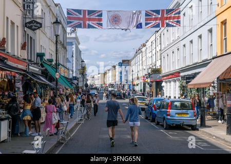 London England - 28. Mai 2023: Ein Paar, das sich an den Händen hält, während es die Portobello Road in Notting Hill in England mit vielen Geschäften entlanggeht Stockfoto