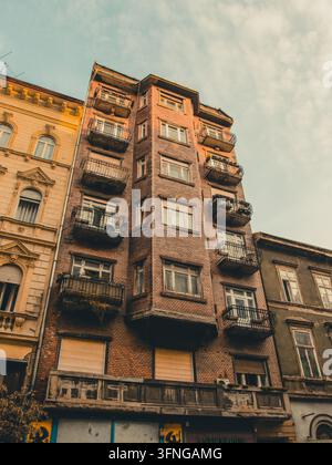Ungarn, Budapest 2019 09 08: Niedrige Ansicht eines alten Vintage-Ziegelwohnhausgebäudes mit Balkonen und Erkerfenstern an einer urbanen Straße. Stockfoto