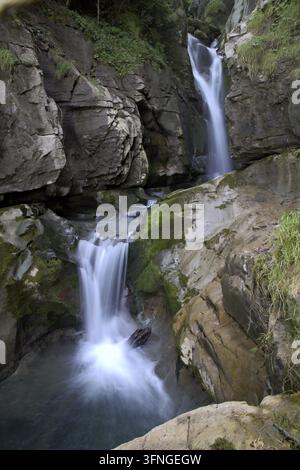 Wasserfall fließt über moosige Felsen in ein klares Becken in einer natürlichen Berglandschaft Stockfoto