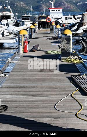 Vertikale detaillierte Makro-Stockfotografie, die einen hölzernen Marina-Pier mit Yachten, Sicherheitsausrüstung und Seilen im Freien bei natürlichem Tageslicht zeigt. Stockfoto