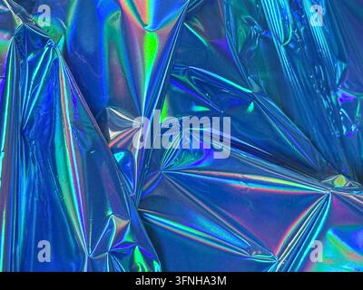 Nahaufnahme einer abstrakten Ansicht von zerknittertem blauem holografischem Material. Reflektierende Oberfläche zeigt lebendige irisierende Regenbogenfarben und scharfe geometrische Falten ill Stockfoto