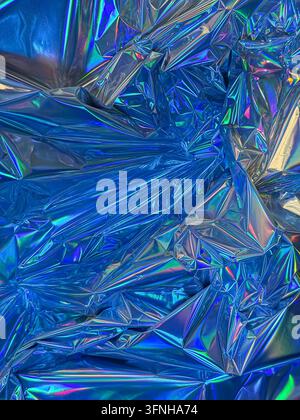 Abstrakter Hintergrund, zerknitterte blaue holografische Folienoberfläche mit irisierenden Regenbogenreflexen und scharfen geometrischen Falten, die eine dynamische, futuristische Wirkung erzeugen Stockfoto