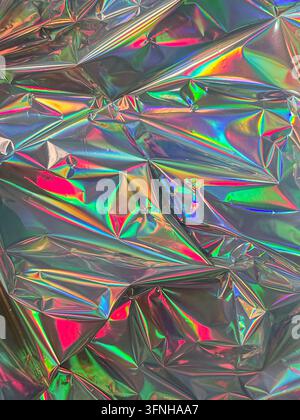 Nahaufnahme zeigt helle Regenbogenfarben, die sich auf zerknitterter Metallfolie spiegeln. Die Textur weist scharfe geometrische Falten und Highlights auf, die eine abstrakte Stockfoto