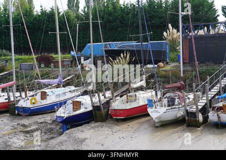 Kleine Yachten und Kajütboote liegen auf dem Schlamm zwischen Holzpfählen in einem Bach in Rye. Rye, England Stockfoto