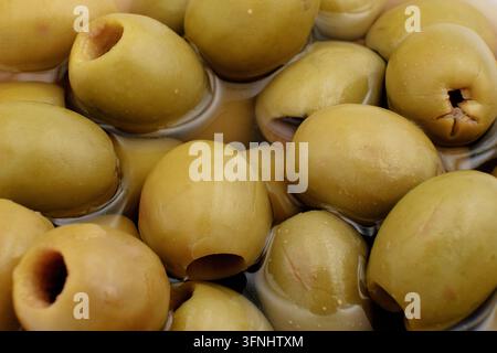 Nahaufnahme von grünen Oliven in Lake mit glänzender Schale und Lichtreflexionen für kulinarische Verpackungen und Rezeptbilder. Stockfoto