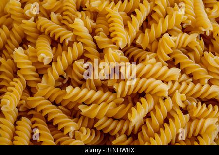 Nahaufnahme von ungekochten Fusilli-Pasta-Spiralen, die das Bild mit einer warmen goldenen Farbe füllen, repetitive Textur Stockfoto