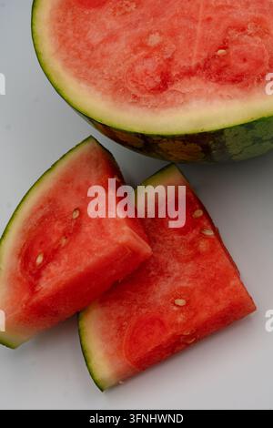 Nahaufnahme von geschnittenen Wassermelonenkeilen und einer Melonenhälfte, die rotes saftiges Fruchtfleisch, grüne Schale und Samen zeigen, für sommerliche Obstfrische heute Stockfoto