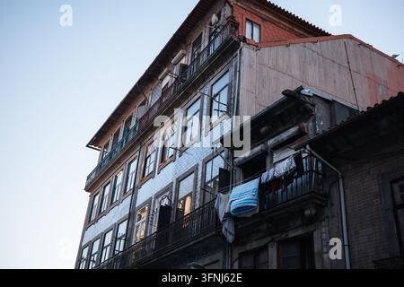 Niedriger Blick auf ein altes Wohnhaus in Porto, Portugal, mit gekachelten Wänden, schmiedeeisernen Balkonen, verwitterten Fenstern, hängender Wäsche, Stockfoto
