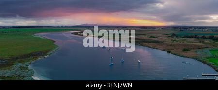 Luftaufnahme von ruhigem Wasser und festgemachten Booten entlang der Küste von Werribee South, Victoria, Australien, unter dramatischen Wolken und einem farbenfrohen Sonnenuntergang über Stockfoto