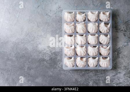 Tiefgekühlte Fertiggerichte asiatischen potstickers Klöße zu kochen von Garnelen in Kunststoffbox über grau Textur Hintergrund gefüllt. Ansicht von oben, Platz. Halbzeug Stockfoto