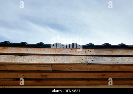 Eine detaillierte Nahaufnahme einer dunkelgrünen, welligen Metalldachinstallation über horizontalen Holzplanken, aus einem niedrigen Winkel gegen ein weiches, o Stockfoto