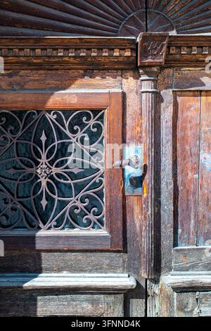 Diese verwitterte Holztür, die 1830 gefertigt wurde, zeigt kunstvolle Metallschmiedearbeiten und historische architektonische Details und dient als zeitlose Eingangstür Stockfoto