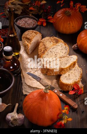Warme, rustikale Herbst-Stillleben mit geschnittenem Vollkornbrot mit Sesamsamen, kleinen orangefarbenen Kürbissen, Olivenöl und verschiedenen Gewürzen, arrangiert auf Stockfoto