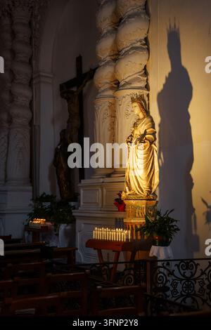 Leuchtende Statue der Jungfrau Maria mit dramatischem Schatten im schwach beleuchteten Kircheninneren, religiöser Glaube, spirituelles Gebet, traditioneller christlicher Gottesdienst, Kirche der Heiligen Katharina von Alexandrien in der Stadt Taormina Stockfoto