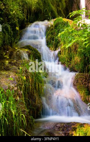 Kleine Kaskaden fließen über kalkige Tuffterrassen und durch üppige Vegetation unterhalb des Uracher Wasserfalls nahe Bad Urach in der Schwäbischen Alb. Stockfoto