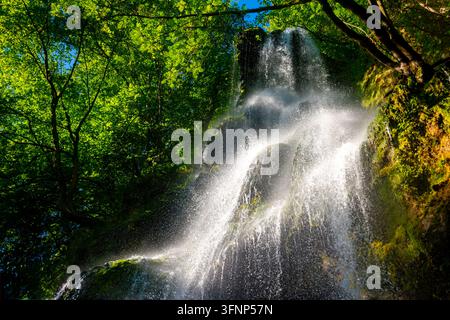 Sonnenbeschienener Uracher Wasserfall stürzt über moosbedeckte Felsen in einem üppigen grünen Wald nahe Bad Urach in der Schwäbischen Alb, Baden-Württemberg, Deutschland. Stockfoto