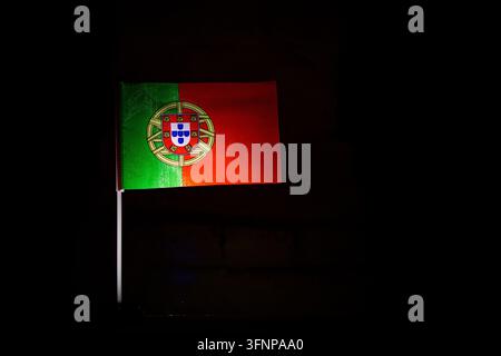 Portugiesische Flagge mit Armillarsphäre und Wappen steht lebhaft im engen Nachtlicht, der Stoff weht über eine schwarze Umgebung und gibt Kopierraum für Text Stockfoto