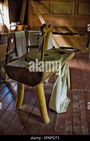 Eine manuelle Holzmasermühle mit einem runden Steinquern, montiert auf einem rustikalen Holzständer über Holzdielen in einem alten ländlichen Gebäude. Stockfoto
