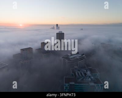 Hochhäuser durchstechen eine dicke Decke aus Morgennebel während des Sonnenaufgangs. Dies ist die Royal Waterside-Anlage in Park Royal, London. Stockfoto