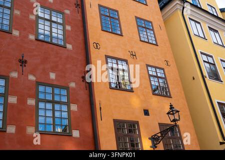 Niedriger Winkel einer farbenfrohen roten, orangefarbenen und gelben historischen Gebäudefassade mit Glasfenstern, Eisenwandbefestigungen und Straßenlaterne am Stortorget-Platz in Stockfoto