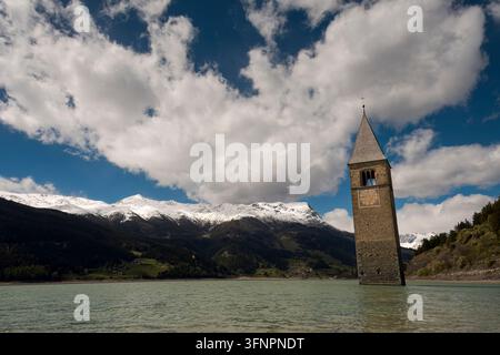 Historischer Glockenturm erhebt sich aus einem alpinen Reservoir unter schneebedeckten Gipfeln (Graun im Vinschgau, Italien: 12-mai-2026) Stockfoto