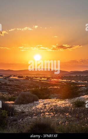 Dramatischer Sonnenuntergang über der Palmwag-Konzession in Damaraland, Namibia. Die lebendigen orangefarbenen und gelben Töne der untergehenden Sonne beleuchten ein weites, arides Land Stockfoto