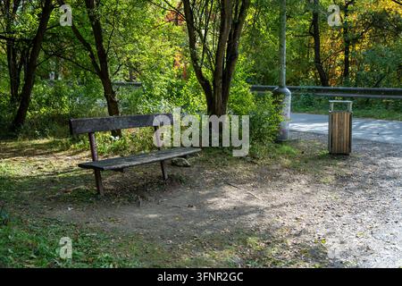 Holzbank und Mülleimer an einem schattigen Rastplatz neben einer Straße im Prokop-Tal. Prag, Tschechien – 4. Oktober 2026. Stockfoto