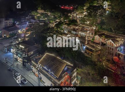 Chongqing, China - 10. Jun 2026 - Kaskadenartig den nächtlichen Hang hinunter fließend, geschichtete hölzerne Dachvorsprünge und verzierte Balkone leuchten mit einer glühenden Wärme, verwebend Stockfoto