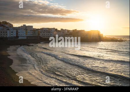 Sonnenuntergang über der Küstenstadt mit weißen Gebäuden und Meereswellen am dunklen Sandstrand, Teneriffa, Kanarischen Inseln, Spanien Stockfoto