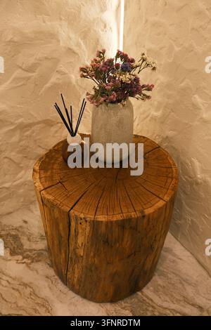 Minimales Interieurelement mit getrockneten Blumen in einer Steinvase und Schwebetropfer auf einem rustikalen Baumstumpf-Tisch, das eine warme natürliche Dekorszene mit Stockfoto