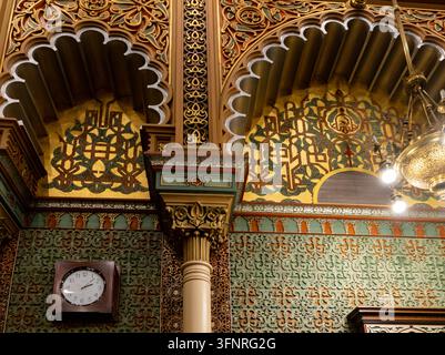 Philadelphia, Pennsylvania - 29. August 2026: Architektonische Nahaufnahme von kunstvollen maurischen Stuckverzierungen, gebogenen Bögen, einer Wanduhr und einem Kronleuchter Stockfoto