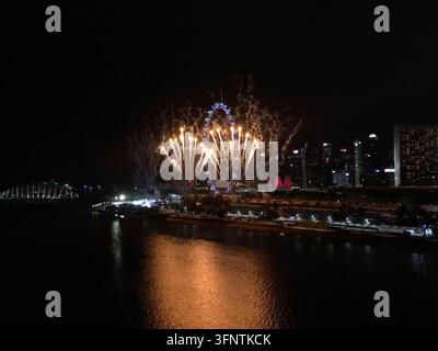 Feuerwerke erhellen den Nachthimmel über der Marina Bay in Singapur. Das Singapore Flyer, ein riesiges Riesenrad, ist im Hintergrund zu sehen, umgeben b Stockfoto